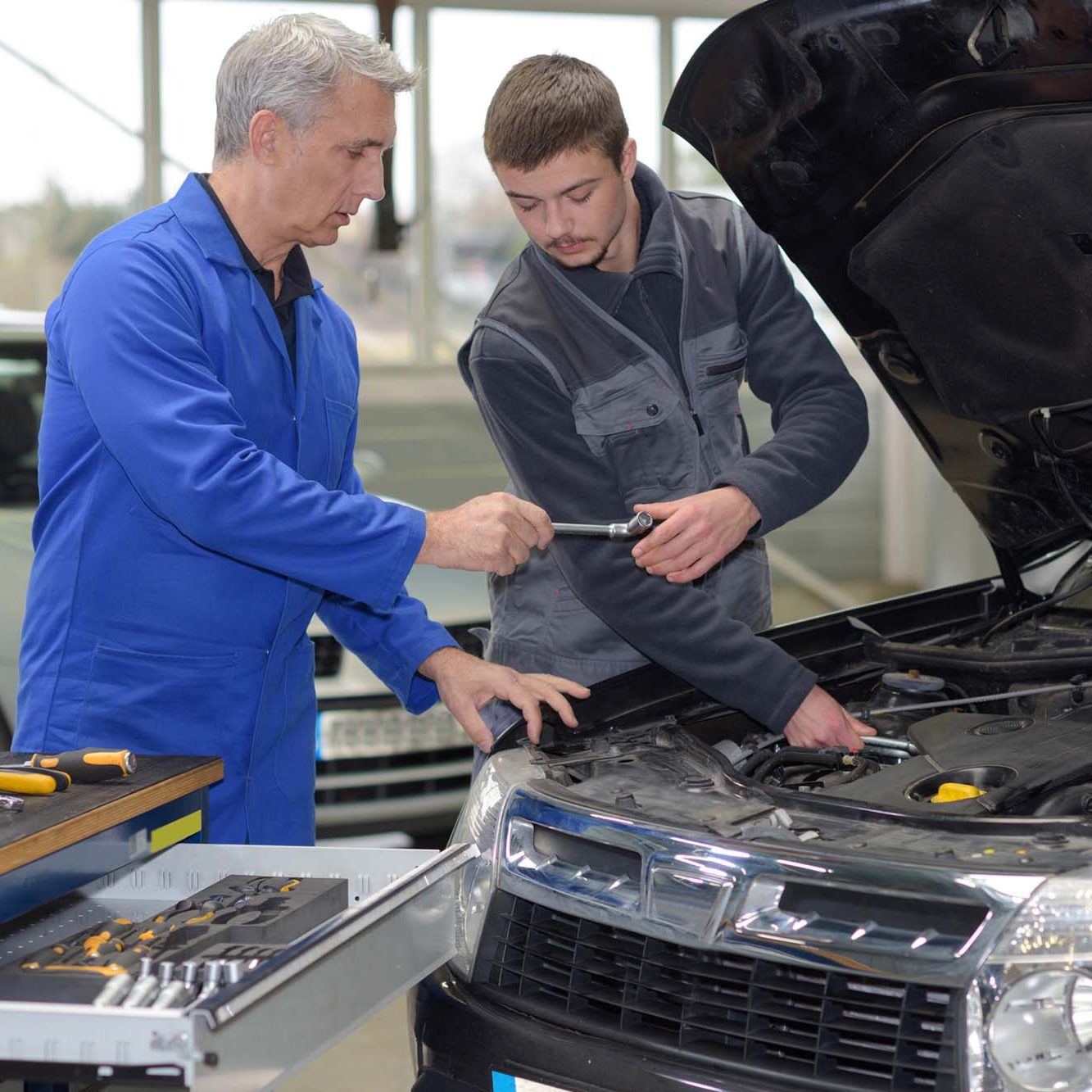 Student mechanic learning from teacher in automotive vocational school trainee