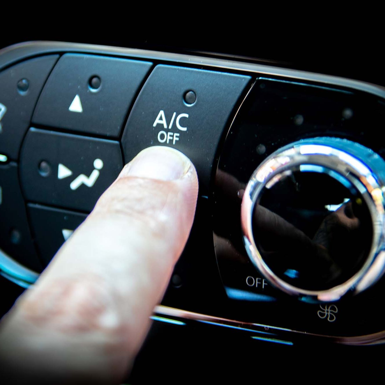 A finger pressing the A/C or air conditioning button on the dashboard of a car
